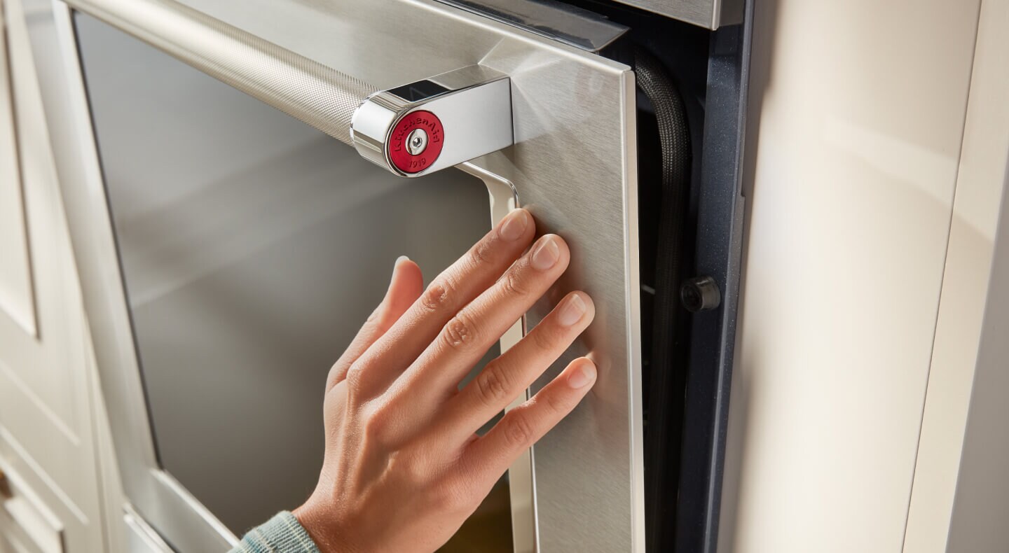 A hand touching a stainless steel oven door with a glass window in it