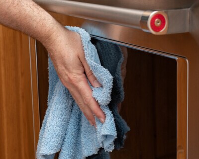 A close up image of oven door glass with a hand buffing it with a rag in the foreground