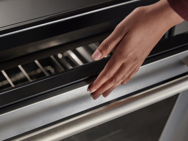 A person lightly touching an oven; the oven door glass is visible just below the person’s hand