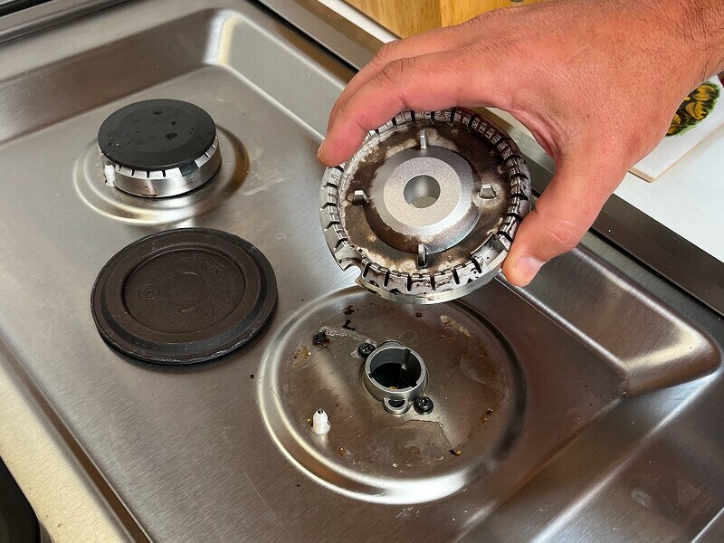 A hand removing a burner base from a gas stovetop