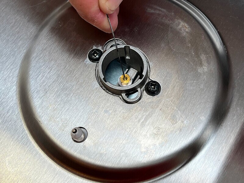 A hand shown clearing debris from a gas tube opening with a needle