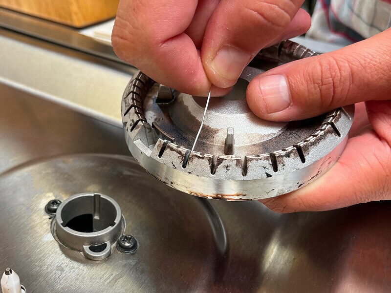 A hand shown cleaning clogged burner ports with a needle