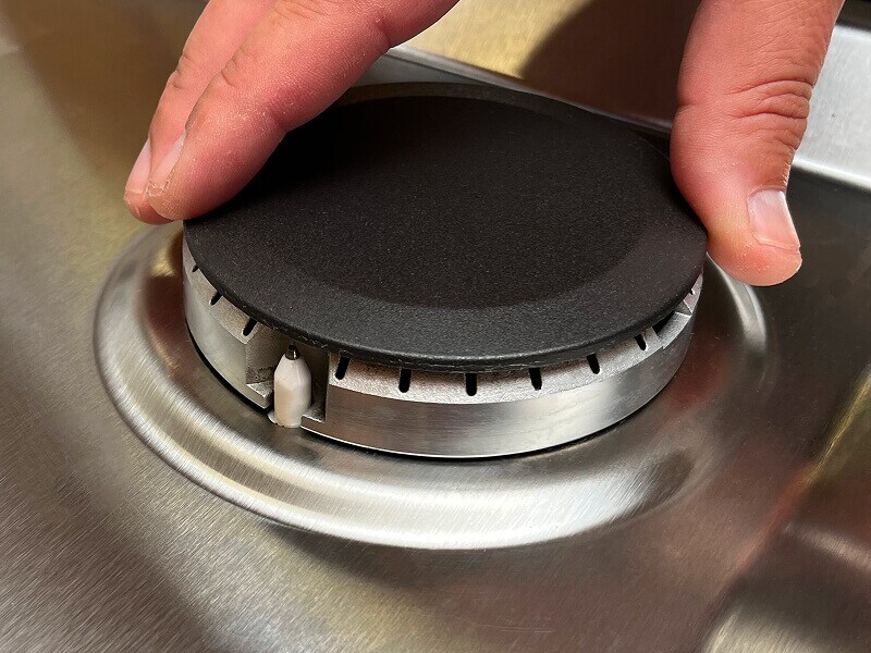 A hand shown replacing the burner cap on a gas stove