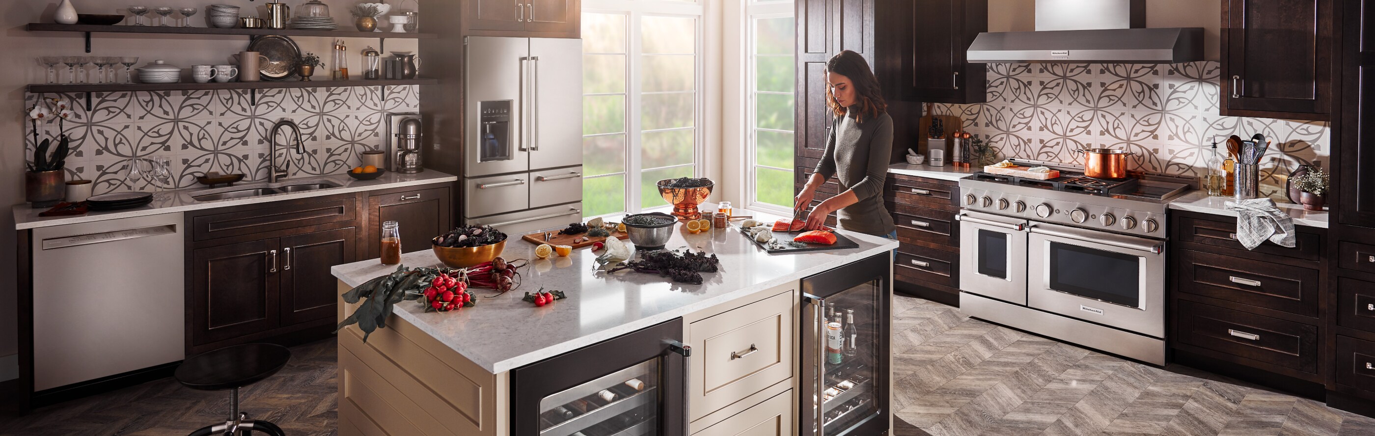 A person making a meal in a modern kitchen next to a KitchenAid® refrigerator.