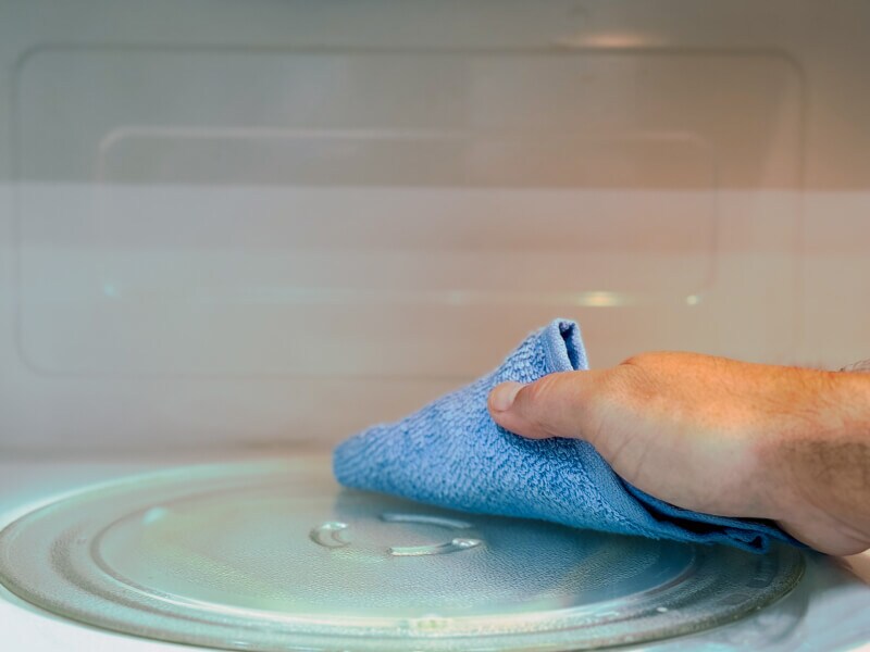 A hand using a damp cloth to finish cleaning the inside of a microwave oven