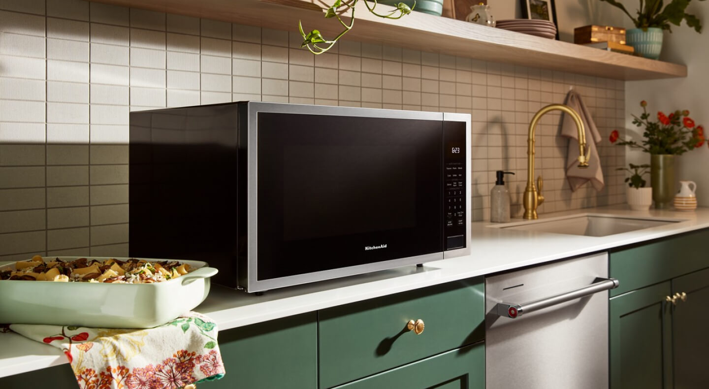 A microwave oven sitting on top of the counter in a kitchen with green cabinetry