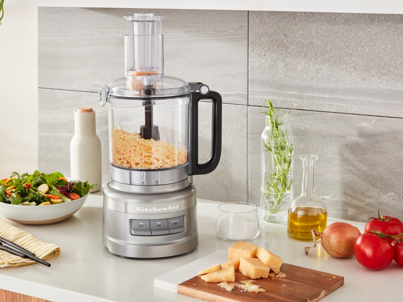 Shredded cheese in a food processor next to a salad Shredded cheese in a food processor next to a salad
