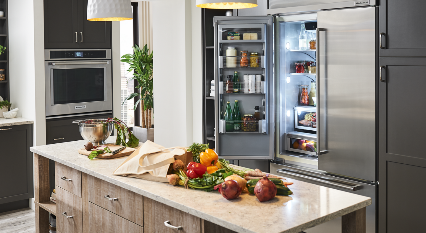Fresh vegetables on countertop and a french door refrigerator behind with doors open