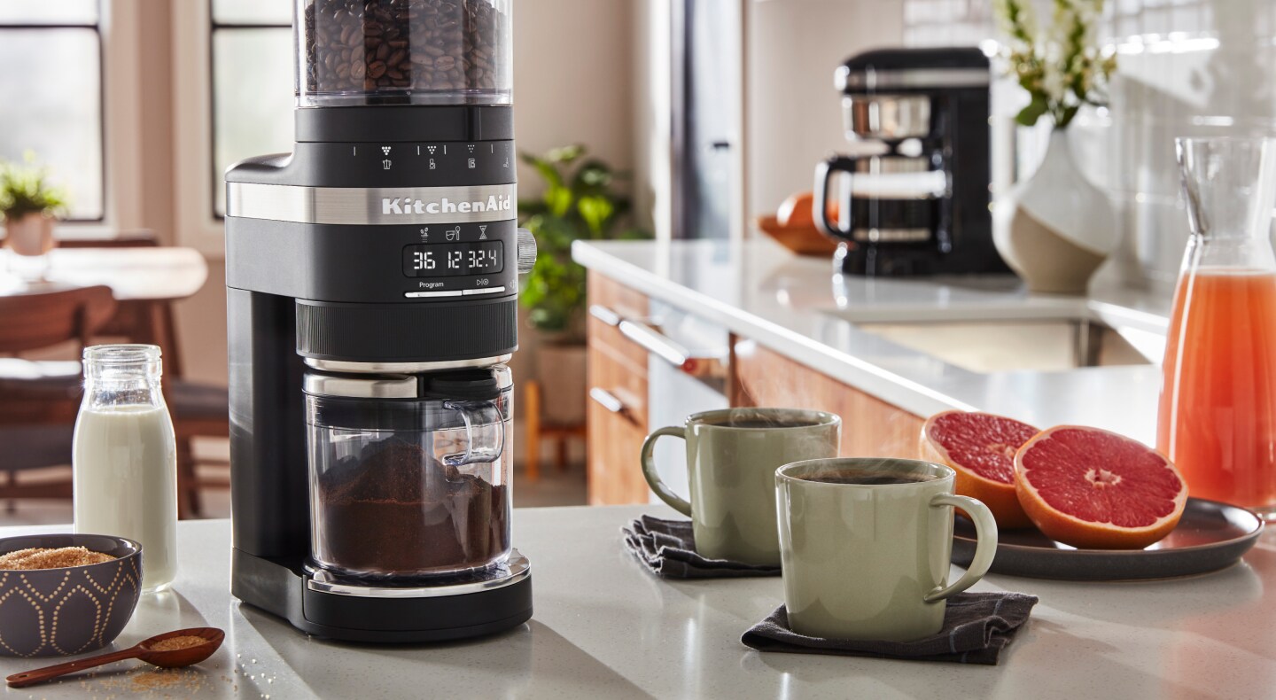 Coffee maker on counter with mugs full of coffee and halved grapefruit pieces Coffee maker on counter with mugs full of coffee and halved grapefruit pieces