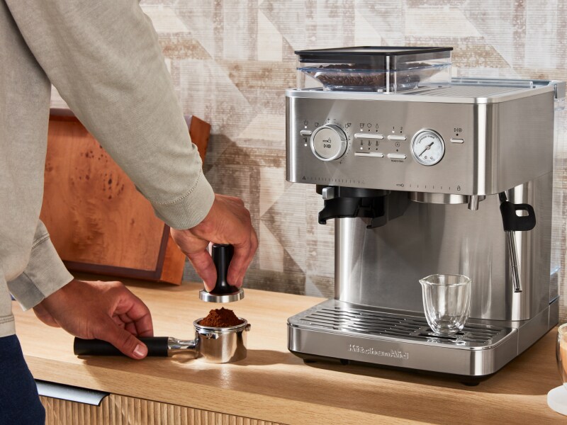 Person tamping espresso next to a KitchenAid® Semi Automatic Espresso Machine