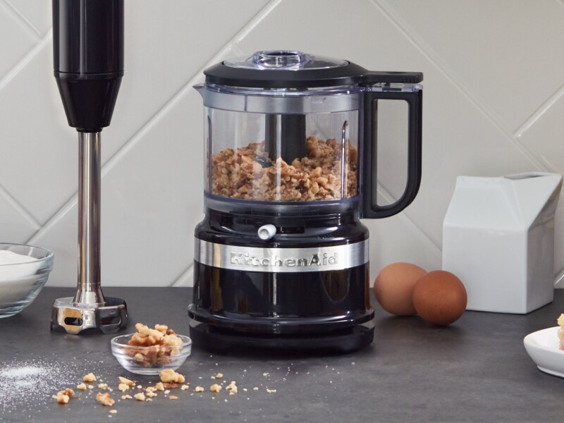Black KitchenAid® food processor filled with walnuts sitting next to an upright immersion blender on a counter Black KitchenAid® food processor filled with walnuts sitting next to an upright immersion blender on a counter