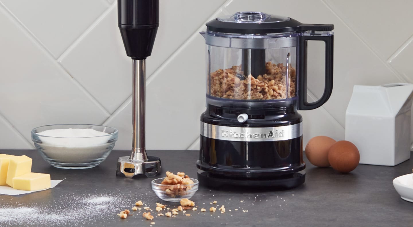 Black KitchenAid® food processor filled with walnuts sitting next to an upright immersion blender on a counter Black KitchenAid® food processor filled with walnuts sitting next to an upright immersion blender on a counter