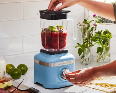 A person using a blue KitchenAid® blender.