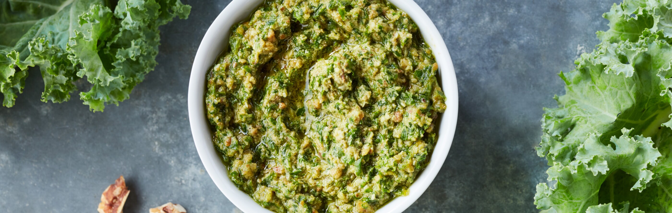 Fresh pesto in a white bowl next to kale