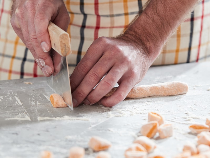 A man cutting pieces of potato gnocchi dough.