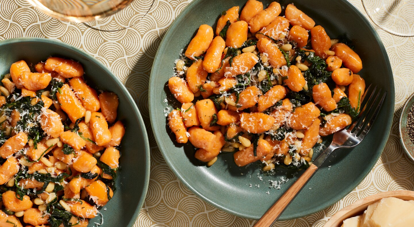 Two bowls of sweet potato gnocchi meals with shaved parmesan, spinach and herbs. Two bowls of sweet potato gnocchi meals with shaved parmesan, spinach and herbs.
