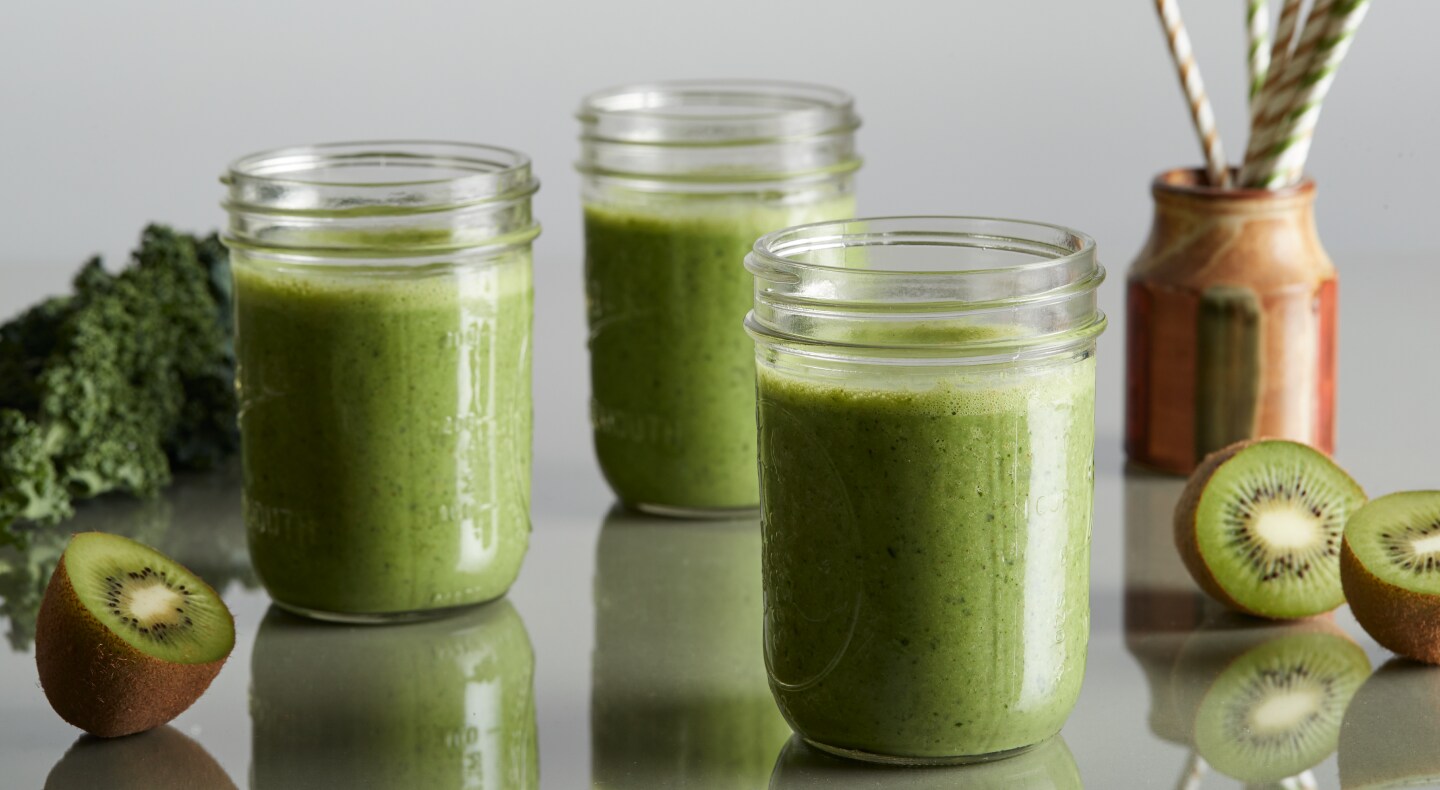 Mason jars of green juice on a countertop next to cut kiwis Mason jars of green juice on a countertop next to cut kiwis