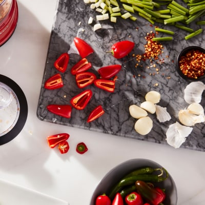 A cutting board on a kitchen counter with sliced peppers and garlic.