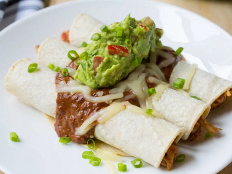 A plate of enchiladas topped with guacamole.  A plate of enchiladas topped with guacamole.