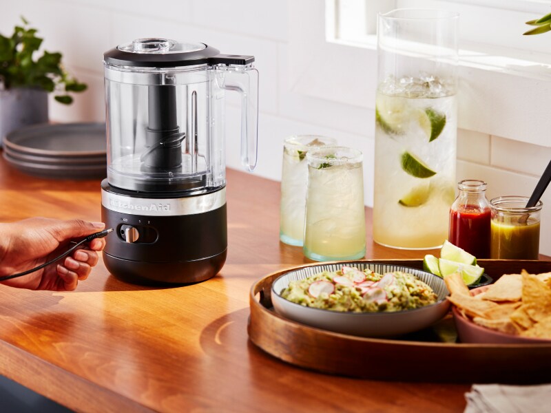 A cordless KitchenAid® food chopper next to a platter of guacamole and tortilla chips and a pitcher and glasses of margaritas.  A cordless KitchenAid® food chopper next to a platter of guacamole and tortilla chips and a pitcher and glasses of margaritas.
