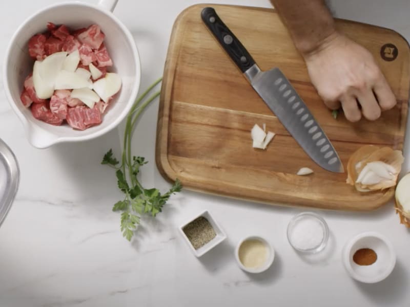 Person slicing onions and adding them to a bowl of raw meat