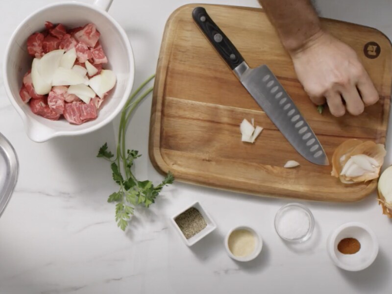 Person slicing onions and adding them to a bowl of raw meat
