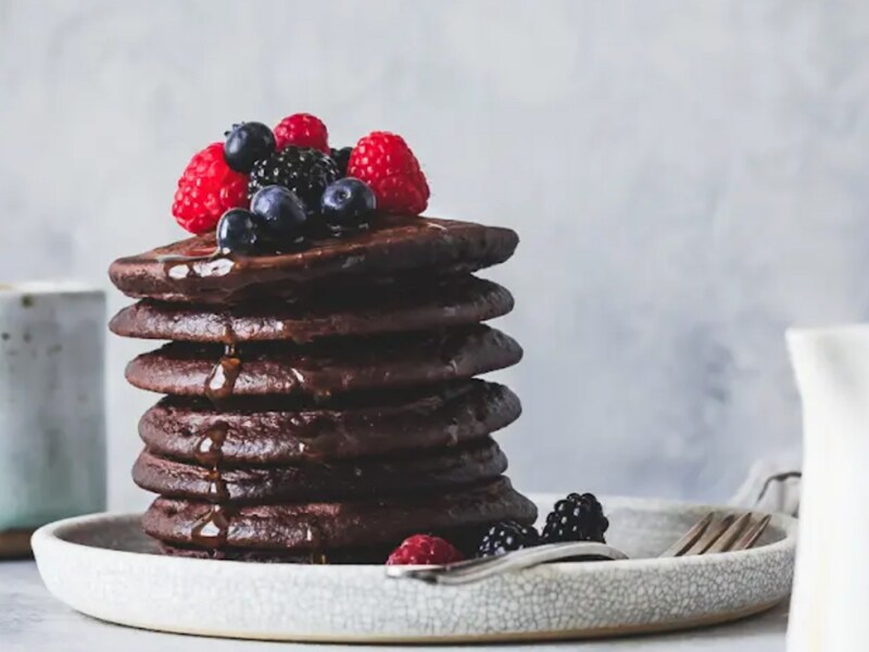 Stack of cocoa pancakes drizzled with syrup and topped with fresh fruit Stack of cocoa pancakes drizzled with syrup and topped with fresh fruit