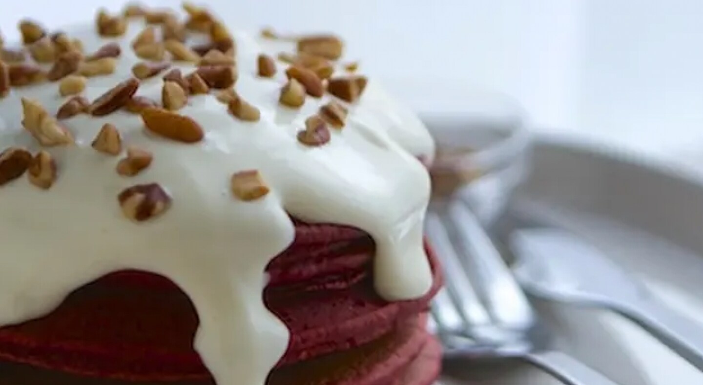 Stack of red velvet pancakes with cream cheese drizzle and nut topping Stack of red velvet pancakes with cream cheese drizzle and nut topping