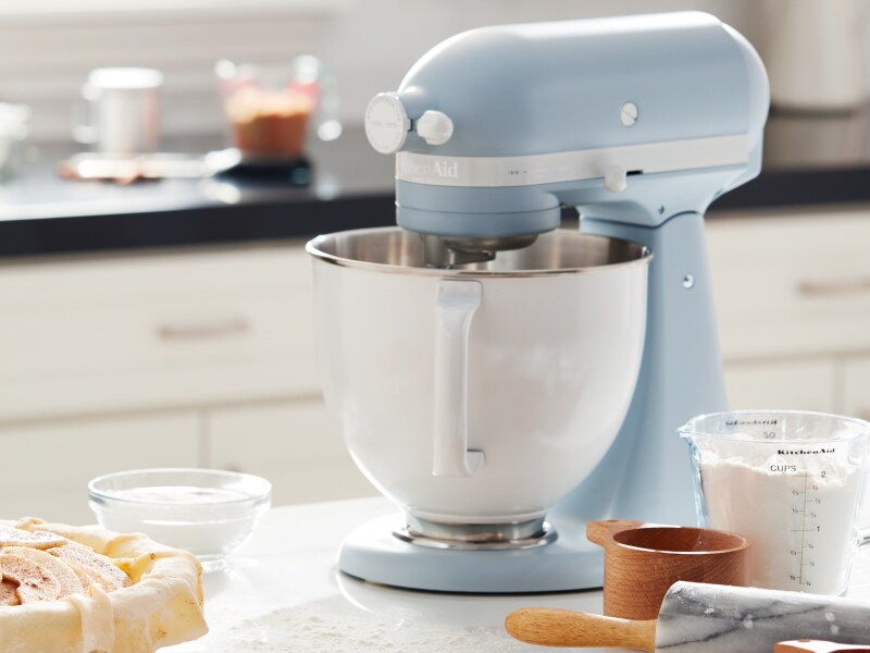Blue KitchenAid® stand mixer on countertop with baking ingredients and plate of cookies Blue KitchenAid® stand mixer on countertop with baking ingredients and plate of cookies