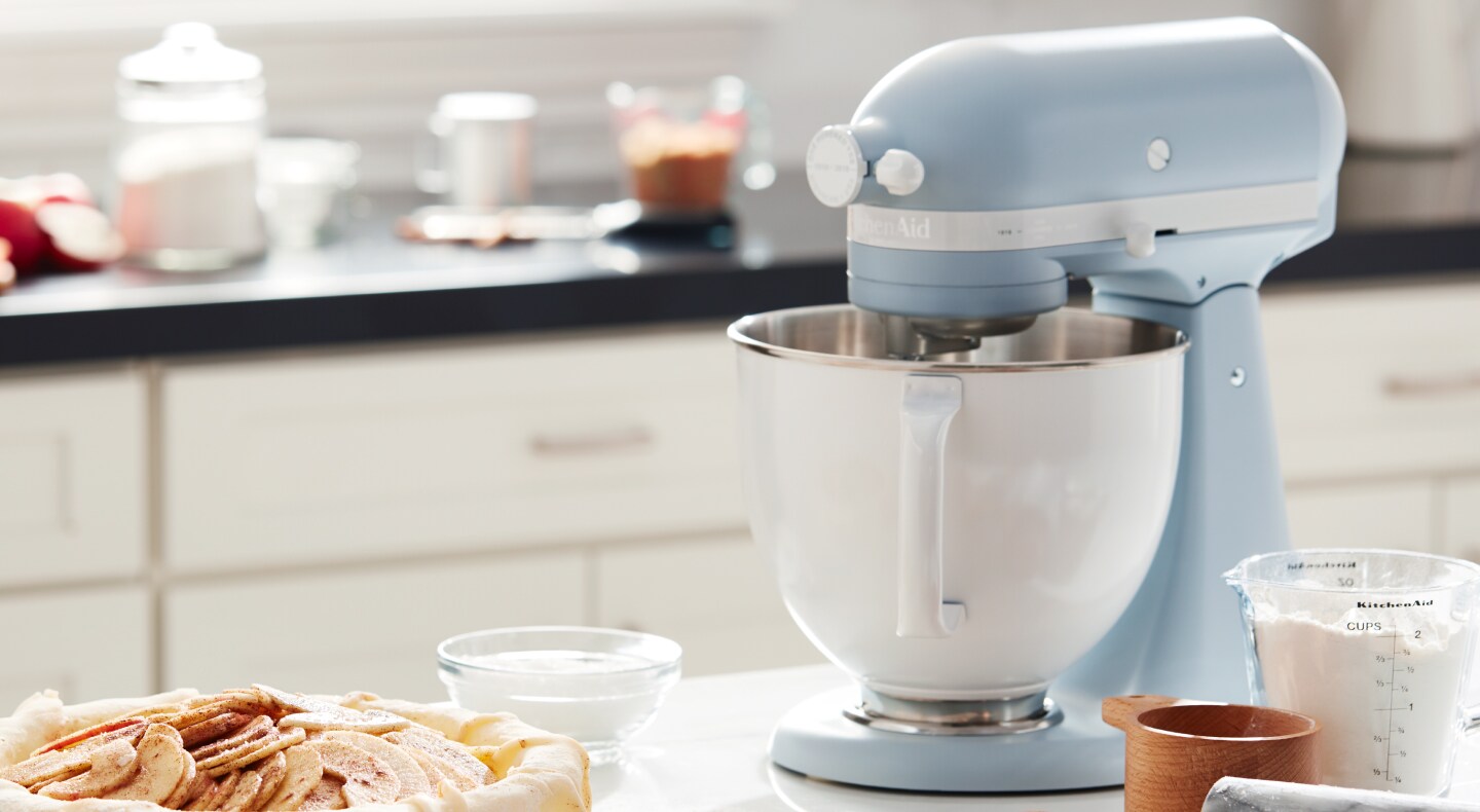 Blue KitchenAid® stand mixer on countertop with baking ingredients and plate of cookies Blue KitchenAid® stand mixer on countertop with baking ingredients and plate of cookies