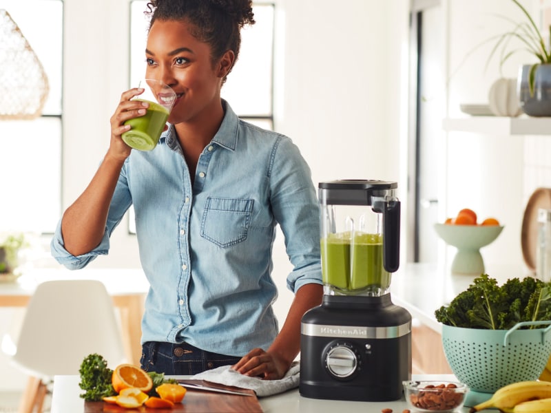 Person drinking a protein shake next to black KitchenAid® blender Person drinking a protein shake next to black KitchenAid® blender