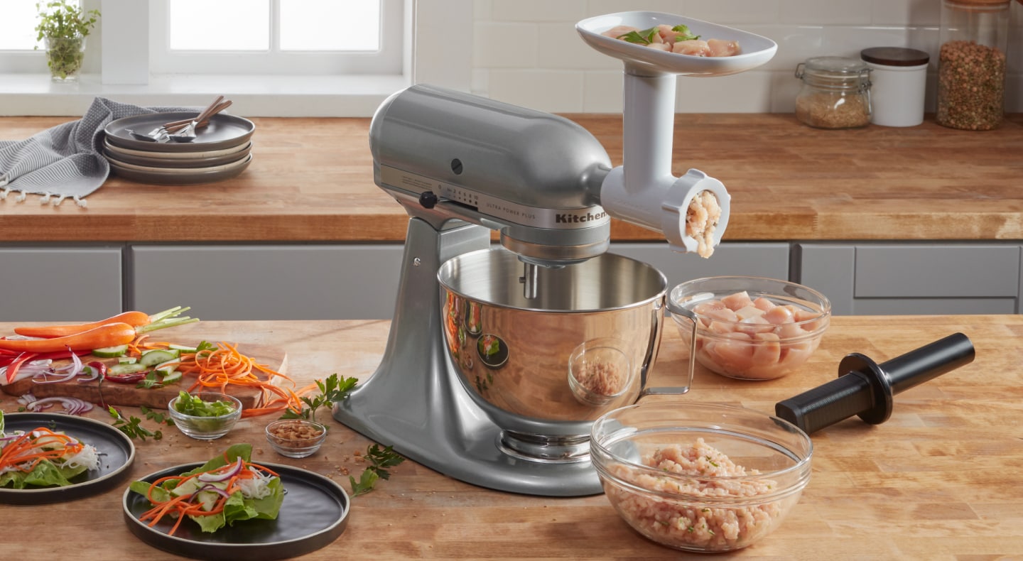KitchenAid® stand mixer with KitchenAid® food grinder attachment and clear bowl of ground chicken KitchenAid® stand mixer with KitchenAid® food grinder attachment and clear bowl of ground chicken