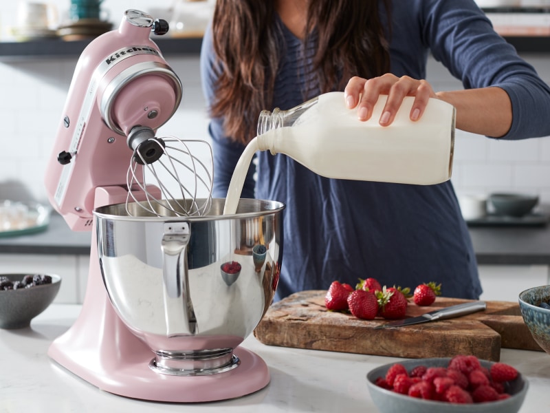 Woman pouring heavy cream into a pink KitchenAid® stand mixer