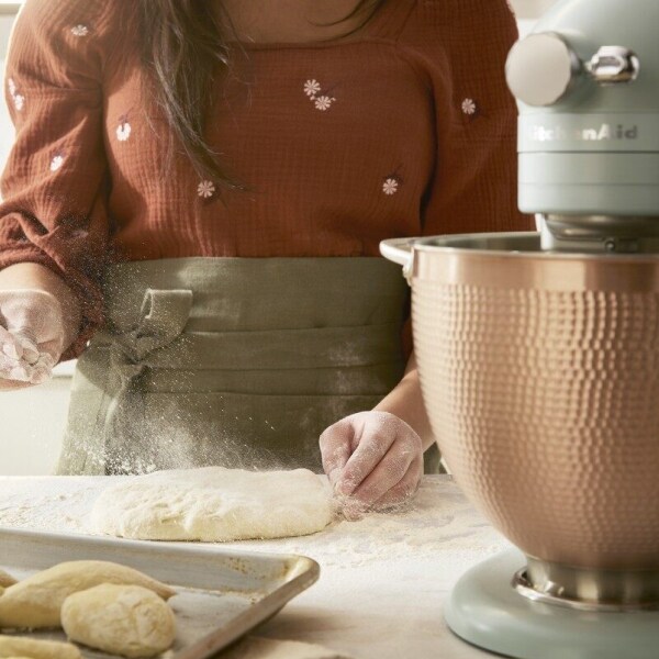 Person dusting bread dough with flour next to a KitchenAid® stand mixer