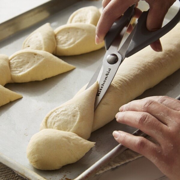 Person using kitchen scissors to score bread dough on a baking sheet