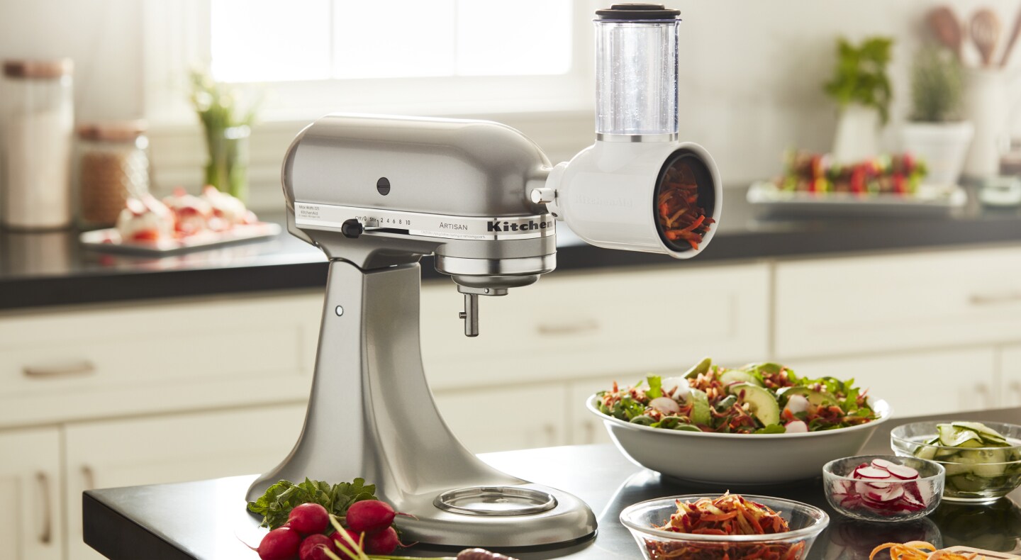 KitchenAid® stand mixer with a fresh prep slicer/shredder attachment in a modern kitchen next to freshly sliced vegetables KitchenAid® stand mixer with a fresh prep slicer/shredder attachment in a modern kitchen next to freshly sliced vegetables