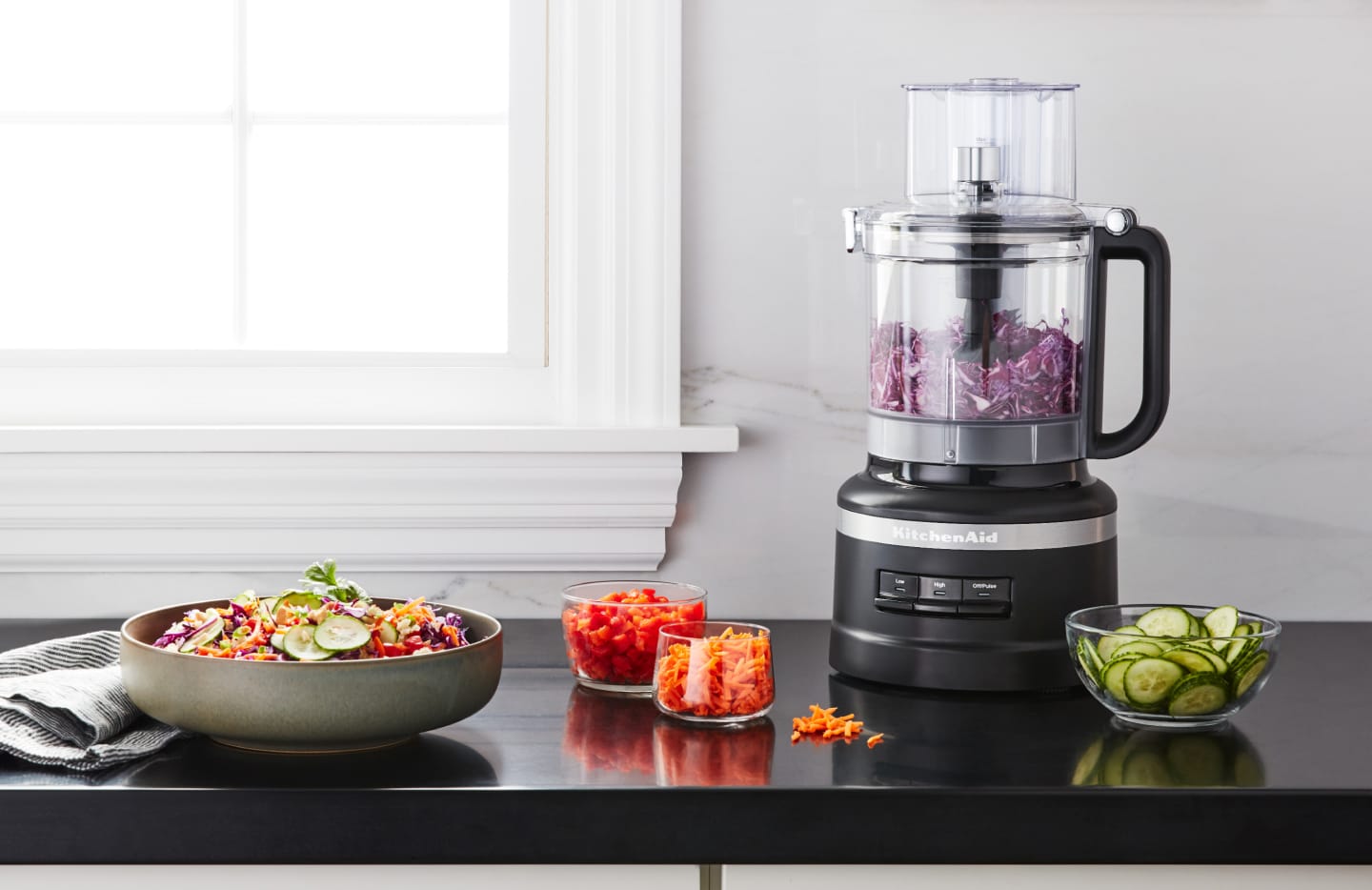 Shredded purple cabbage in a KitchenAid® food processor on a kitchen counter next to other shredded vegetables Shredded purple cabbage in a KitchenAid® food processor on a kitchen counter next to other shredded vegetables