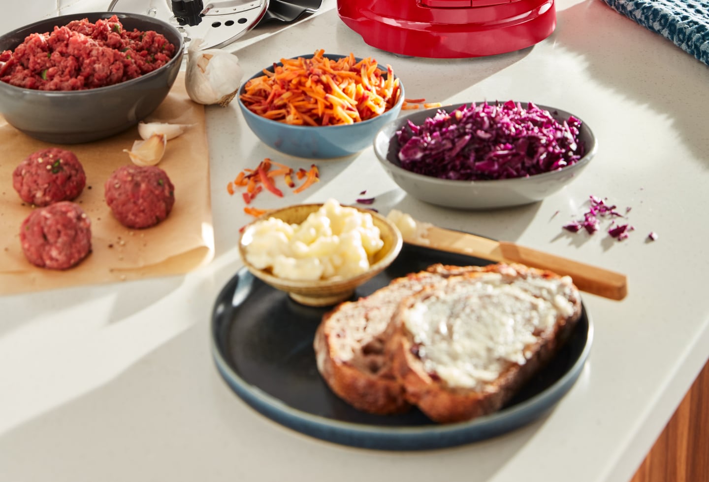 Modern kitchen counter with a bowl of shredded purple cabbage, shredded carrots, garlic cloves, meatballs and a plate of bread with a creamy spread Modern kitchen counter with a bowl of shredded purple cabbage, shredded carrots, garlic cloves, meatballs and a plate of bread with a creamy spread