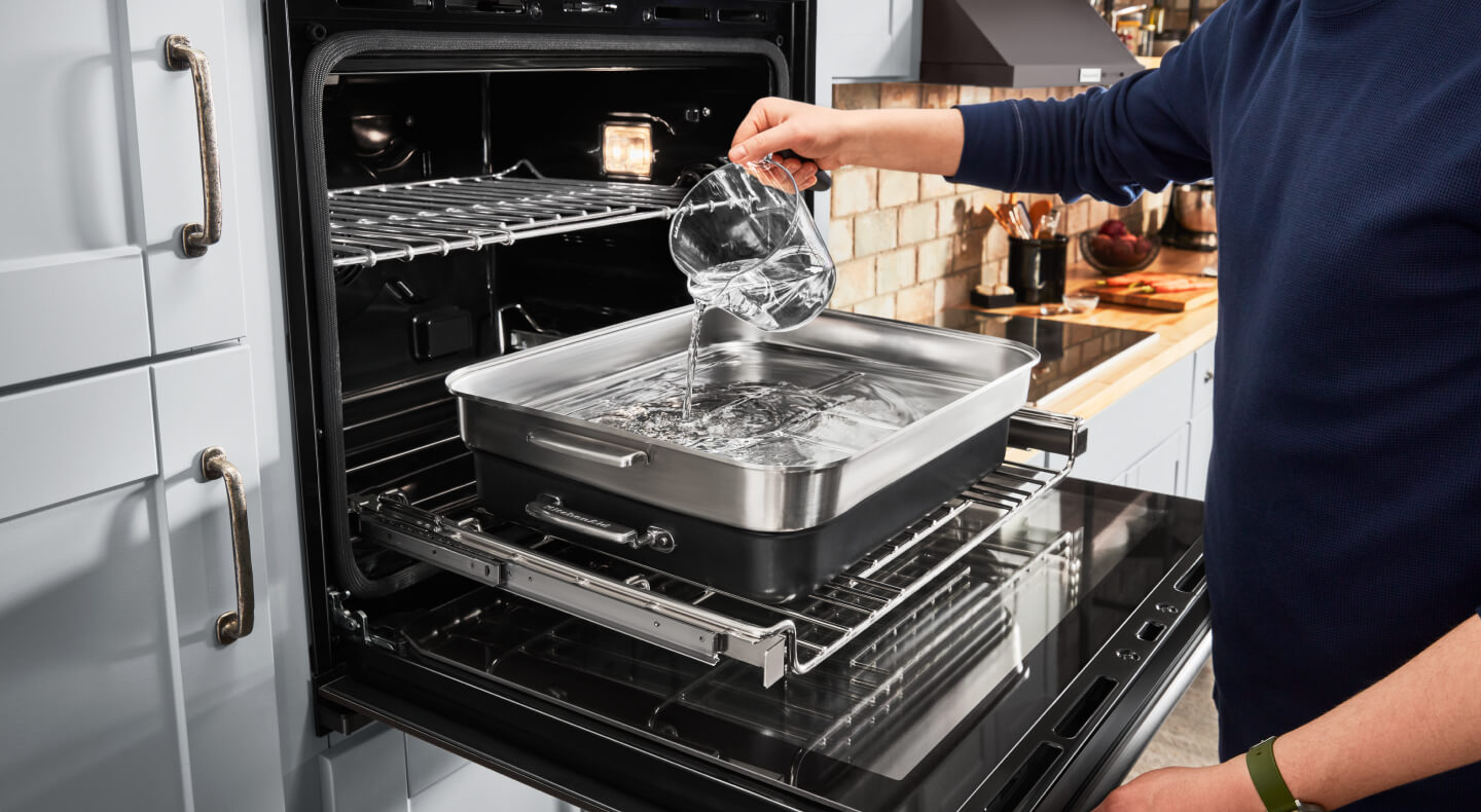 A person putting water in steaming cookware in the oven