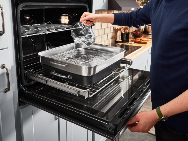 A person putting water in steaming cookware in the oven A person putting water in steaming cookware in the oven
