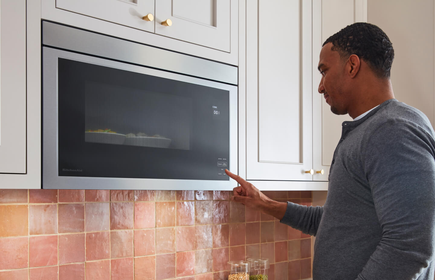 Person selecting a setting on a flush KitchenAid® over-the-range microwave between white cabinets