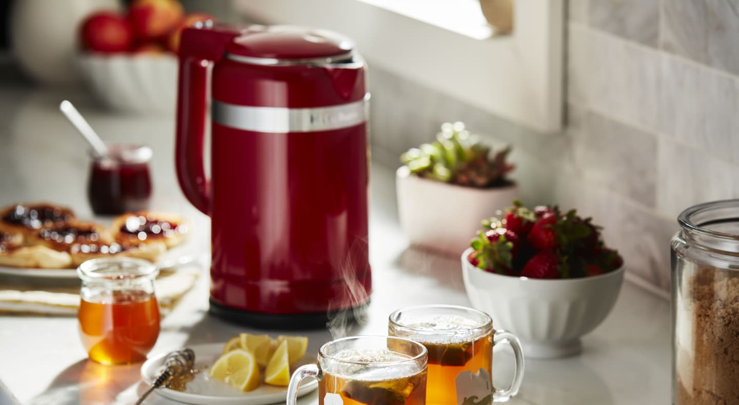 Red KitchenAid® electric kettle on countertop next to glasses of hot tea