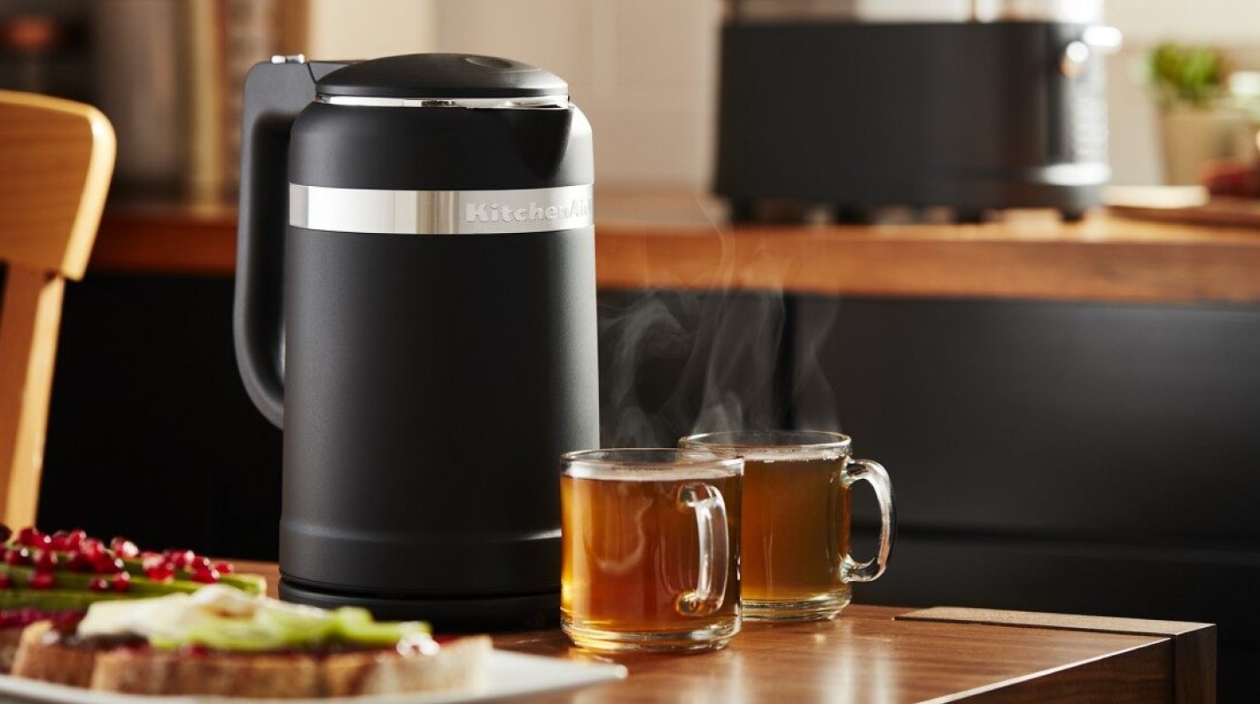 Black KitchenAid® electric tea kettle on table with glasses of tea. Black KitchenAid® electric tea kettle on table with glasses of tea.