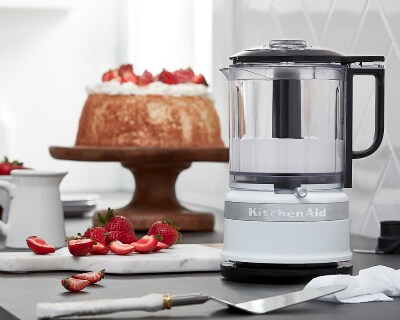 Silver food chopper filled with whipped topping next to cake on counter