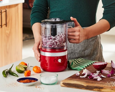 Person pulsing red onions in red food chopper on counter with ingredients