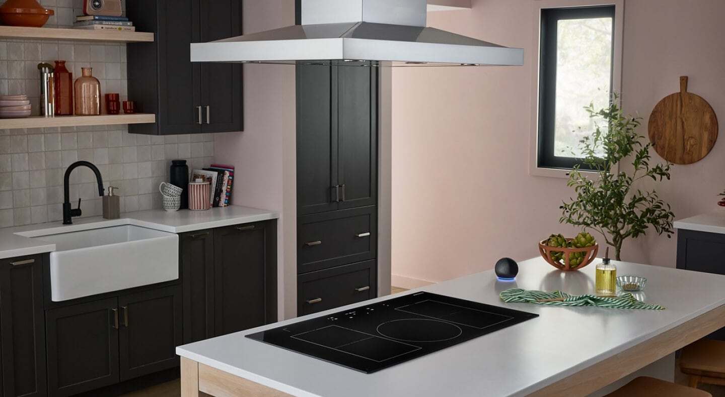A neutral-toned kitchen with an induction cooktop set into an island with a sink and faucet in the background