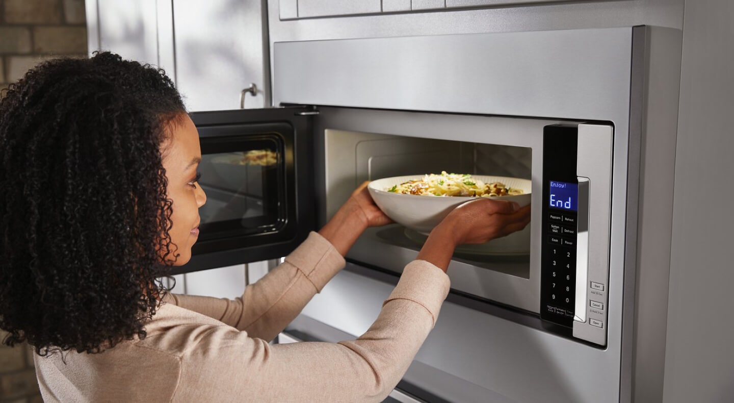 Person taking a bowl of pasta out of a built-in microwave Person taking a bowl of pasta out of a built-in microwave