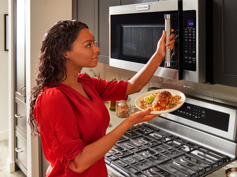Person opening microwave with plate of food in hand Person opening microwave with plate of food in hand