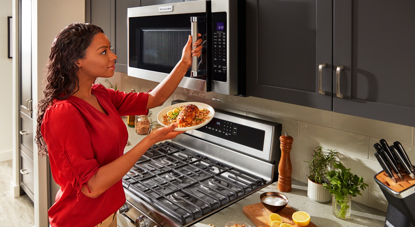 Person opening microwave with plate of food in hand