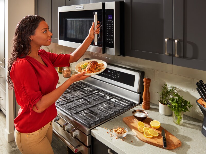 Person opening microwave with plate of food in hand